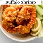 Overhead view of buffalo shrimp in white bowl with celery sticks and lemon slices pin with text overlay.