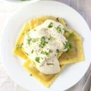 Overhead view of sauce on ravioli on plate.
