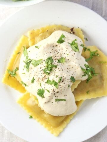 Overhead view of sauce on ravioli on plate.