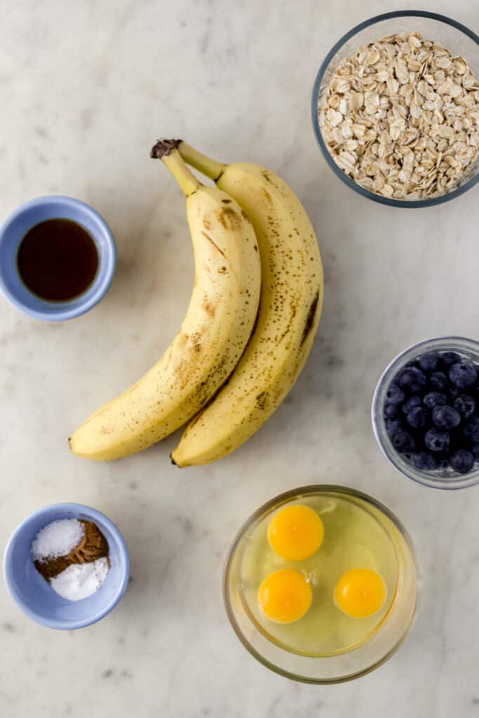 ingredients to make banana pancakes with blueberries on marble surface