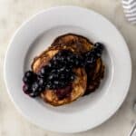 two banana pancakes topped with blueberries on white plate