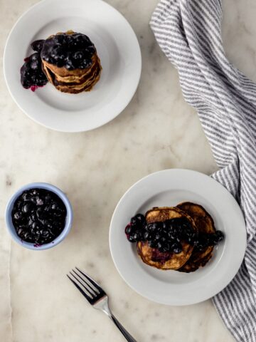 banana pancakes topped with blueberries on white plates with napkin and forks