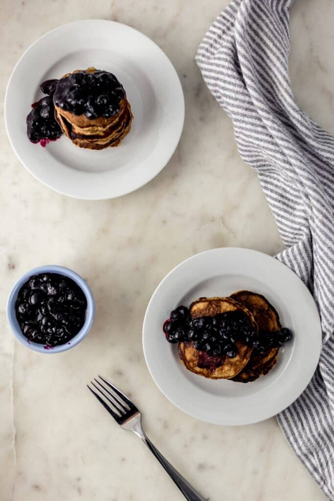 banana pancakes topped with blueberries on white plates with napkin and forks