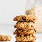 side view of a stack of oatmeal raisin cookies on white surface with glass jar of oats in the background.