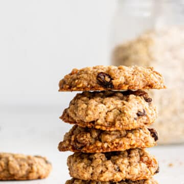 side view of a stack of oatmeal raisin cookies on white surface with glass jar of oats in the background.