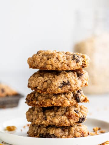 close up side view white plate with a stack of five oatmeal raisin cookies on it.