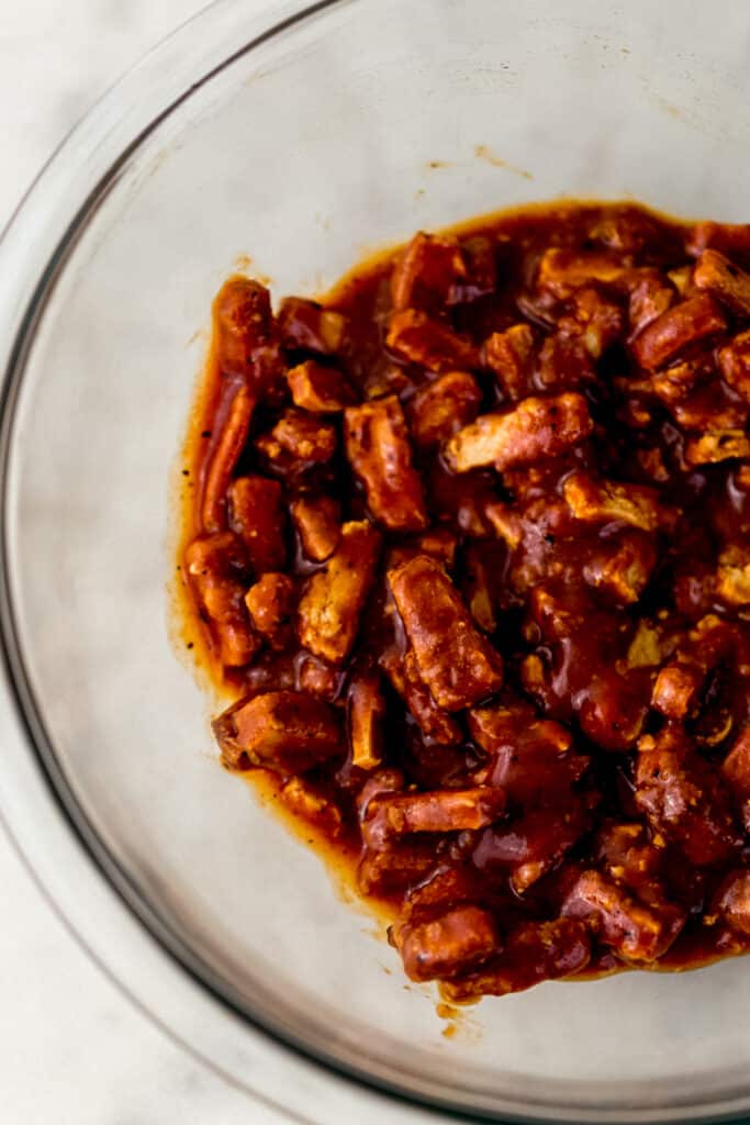 meatless crispy tenders tossed in barbecue sauce in glass mixing bowl. 