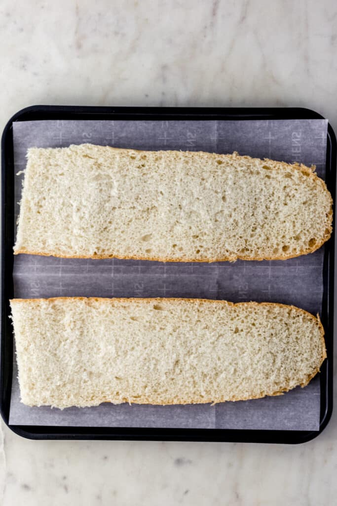 half of French bread loaf cut in half on parchment lined baking sheet 