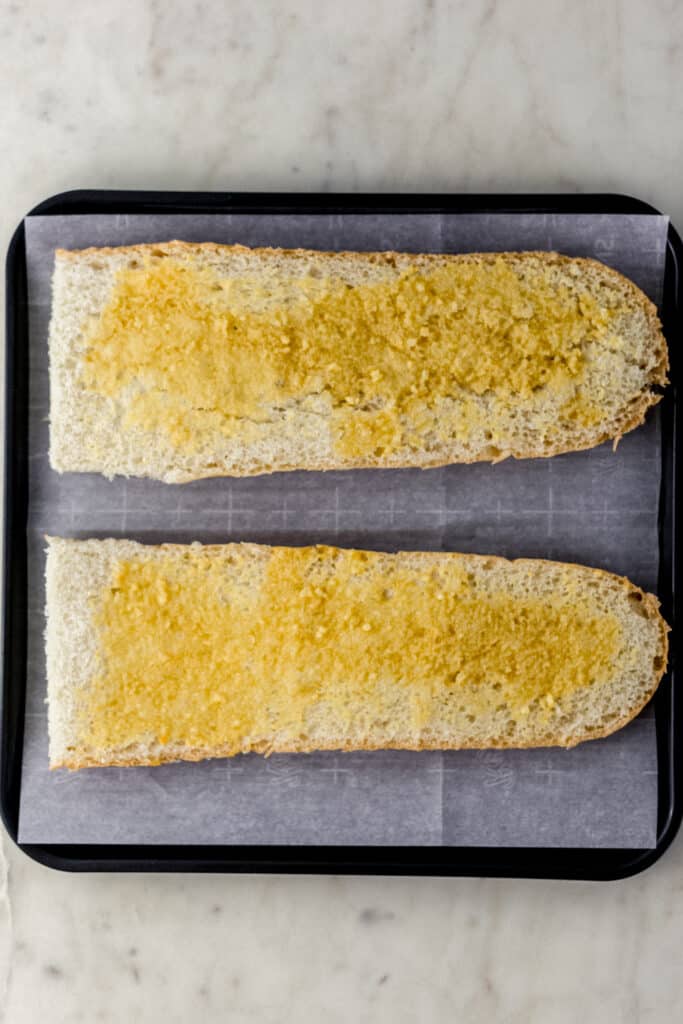 French bread topped with garlic butter mixture before baking on parchment lined baking sheet 