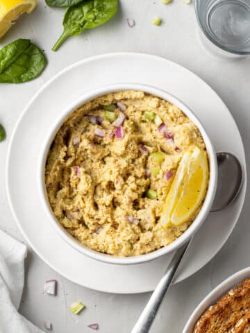 overhead view chickpea salad in white bowl with lemon wedge on white plate with spoon