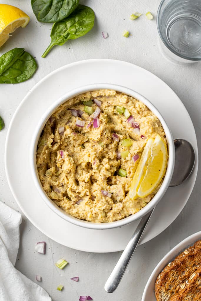 overhead view chickpea salad in white bowl with lemon wedge on white plate with spoon