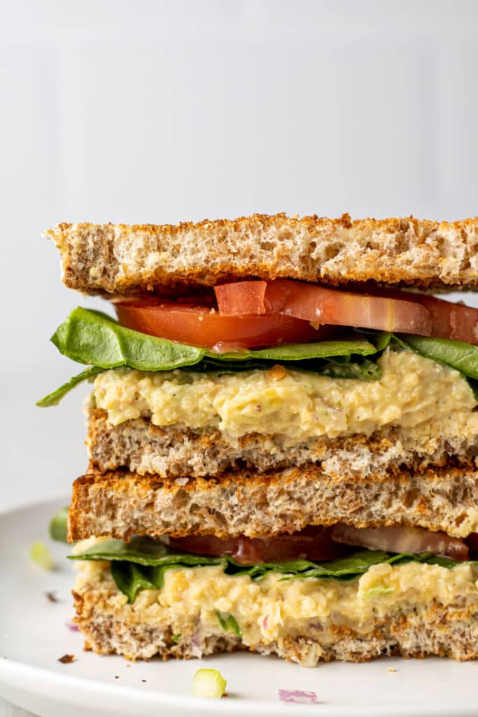 close up side view chickpea sandwich cut in half and stacked on white plate. 