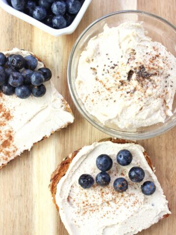 overhead view of glass of cashew butter with two pieces of toast topped with butter and fresh blueberries