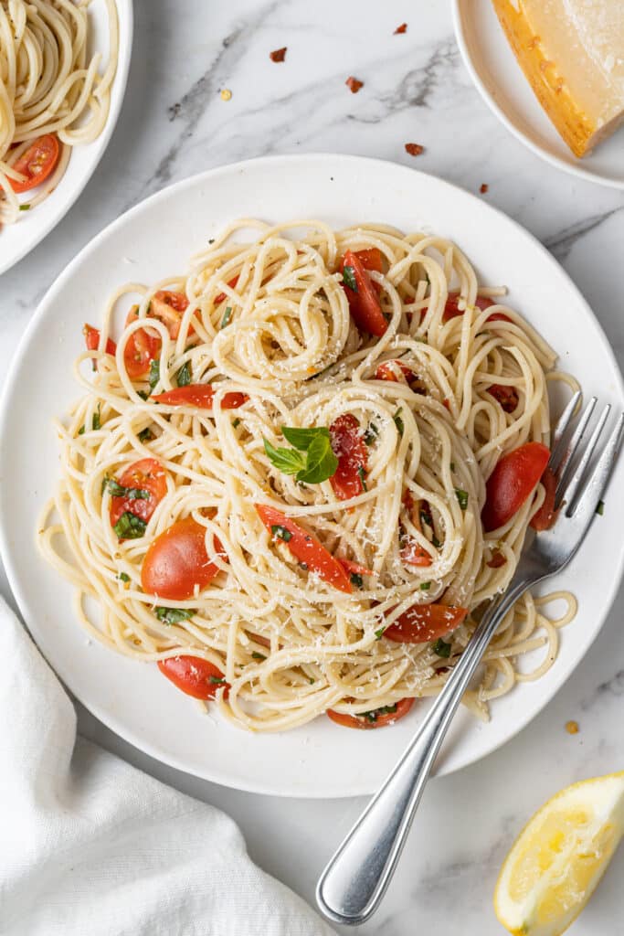 overhead view of pasta and tomato on white plate with fork.