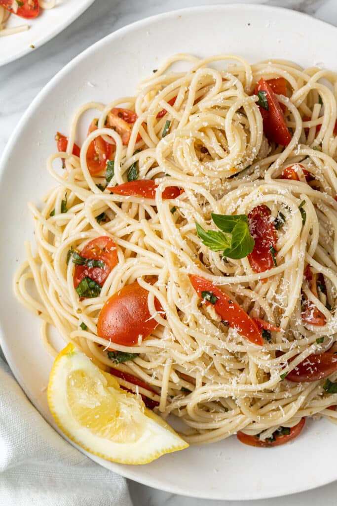 tomato pasta with lemon wedge on white plate topped with parsley. 