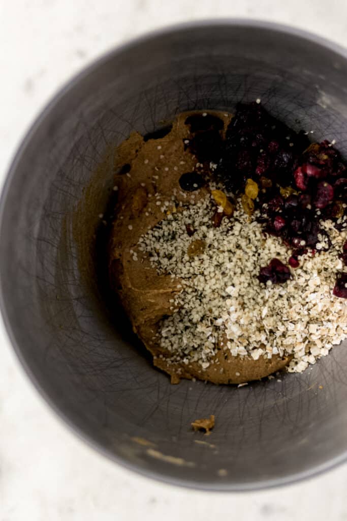 overhead view of oats, seed, and dried fruit added to cookie dough in stand mixer bowl. 