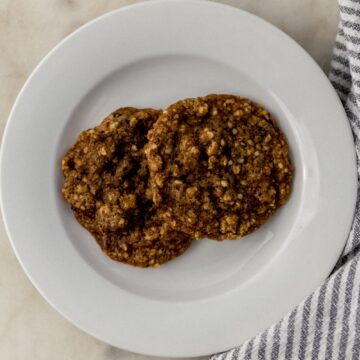 two cookies on a white plate beside a cloth napkin