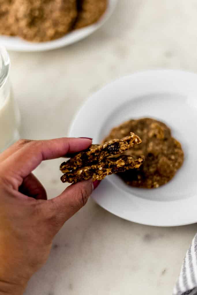 hand holding harvest cookie over white plate with another cookie on it. 