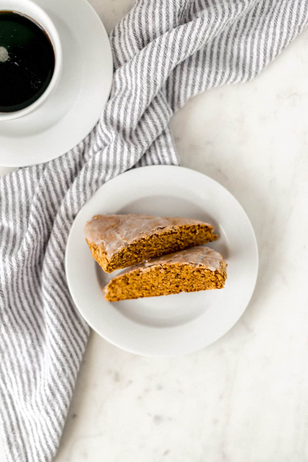 one pumpkin scone cut in half on a white plate next to a cup of coffee and a napkin