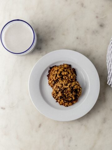 small white plate with two tahini cookies next to cloth napkin and glass of milk