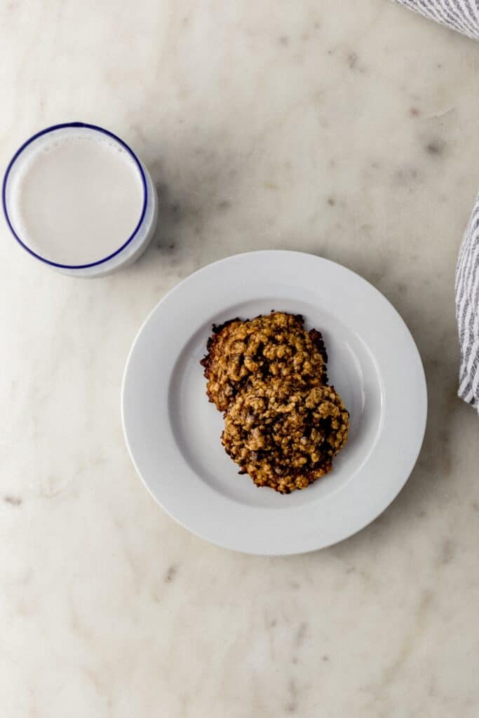 small white plate with two tahini cookies next to cloth napkin and glass of milk
