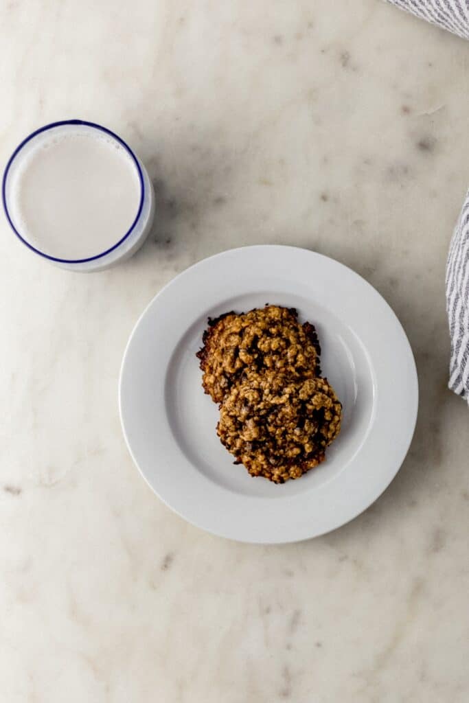 small white plate with two tahini cookies next to cloth napkin and glass of milk 