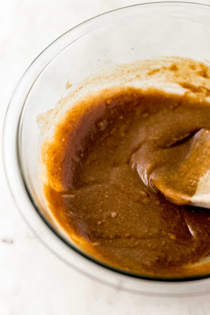 tahini, almond butter, maple syrup, pumpkin spice, and salt mixed together in glass bowl with wooden spoon.