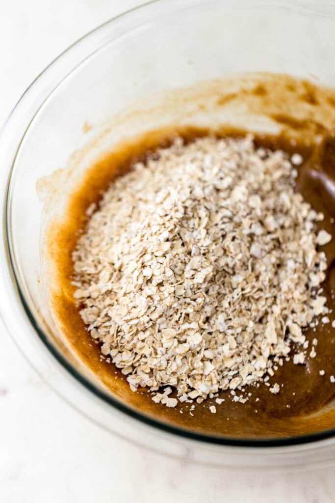 oats added to glass bowl with tahini cookie mixture 