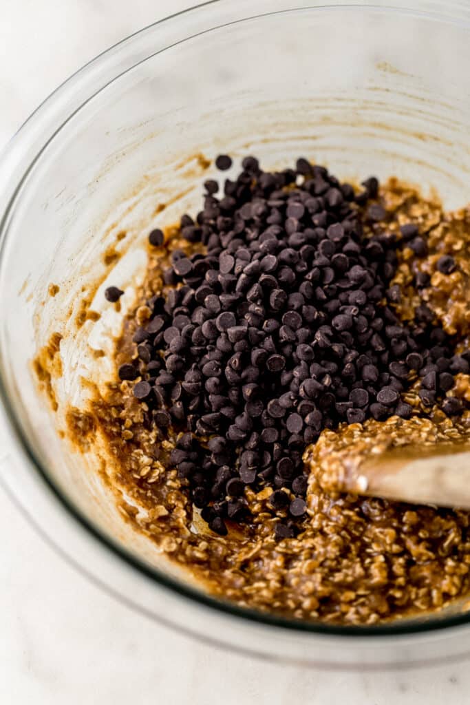 chocolate chips added to glass mixing bowl for cookies with wooden spoon. 