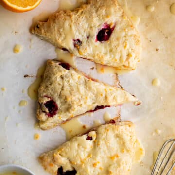 overhead view of three scones on parchment paper with an orange cut in half