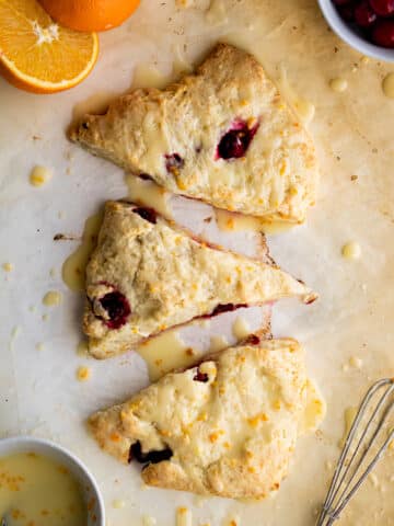 overhead view of three scones on parchment paper with an orange cut in half