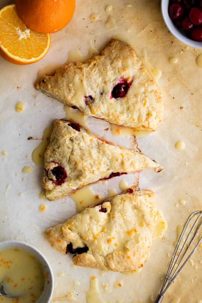 overhead view of three scones on parchment paper with an orange cut in half 