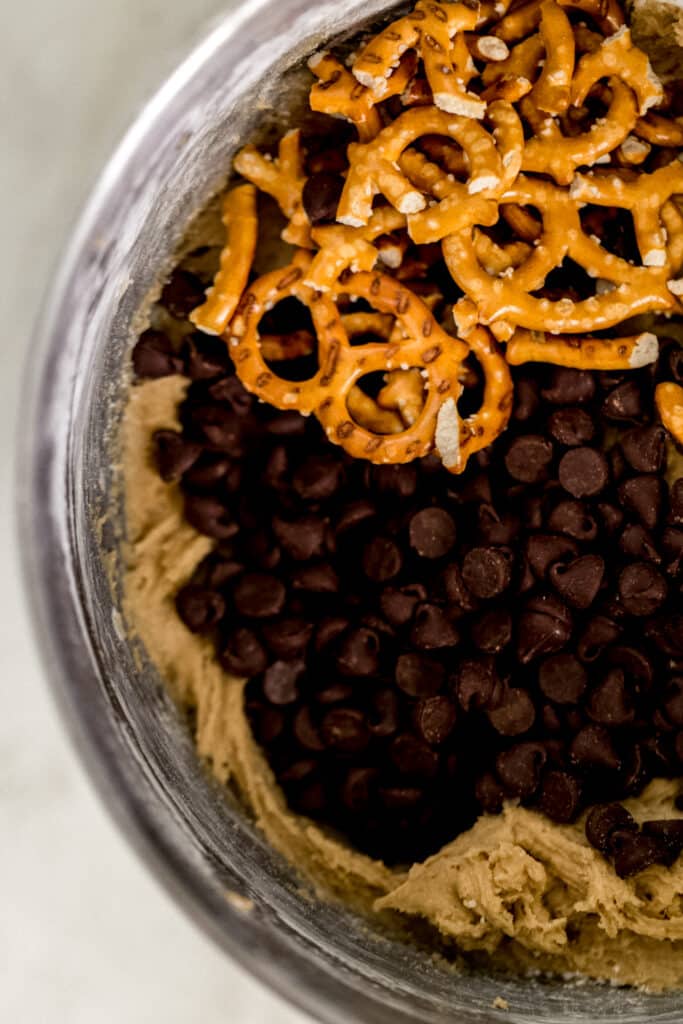 stand mixer bowl with cookie mixture, chocolate chip, and pretzels