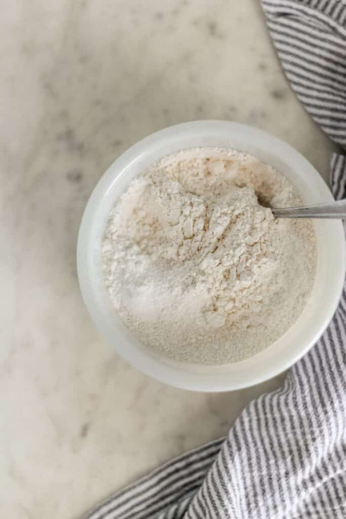 white bowl with flour mixture and spoon beside a napkin 