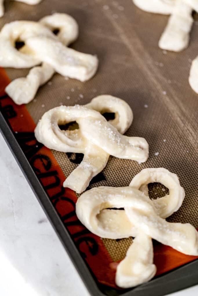 unbaked soft pretzels on sheet pan topped with melted butter and salt