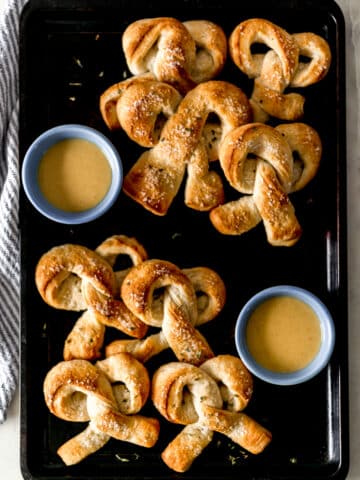 batch of cooked soft pretzels on sheet pan with honey mustard sauce in small blue bowls