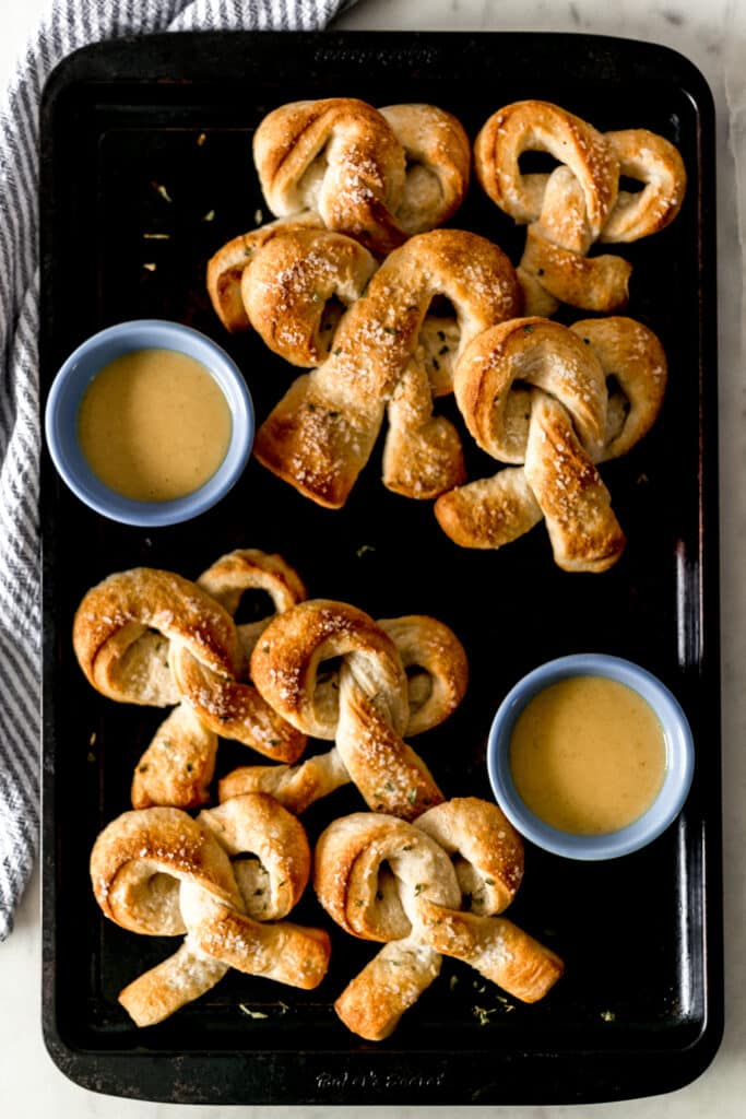 batch of cooked soft pretzels on sheet pan with honey mustard sauce in small blue bowls