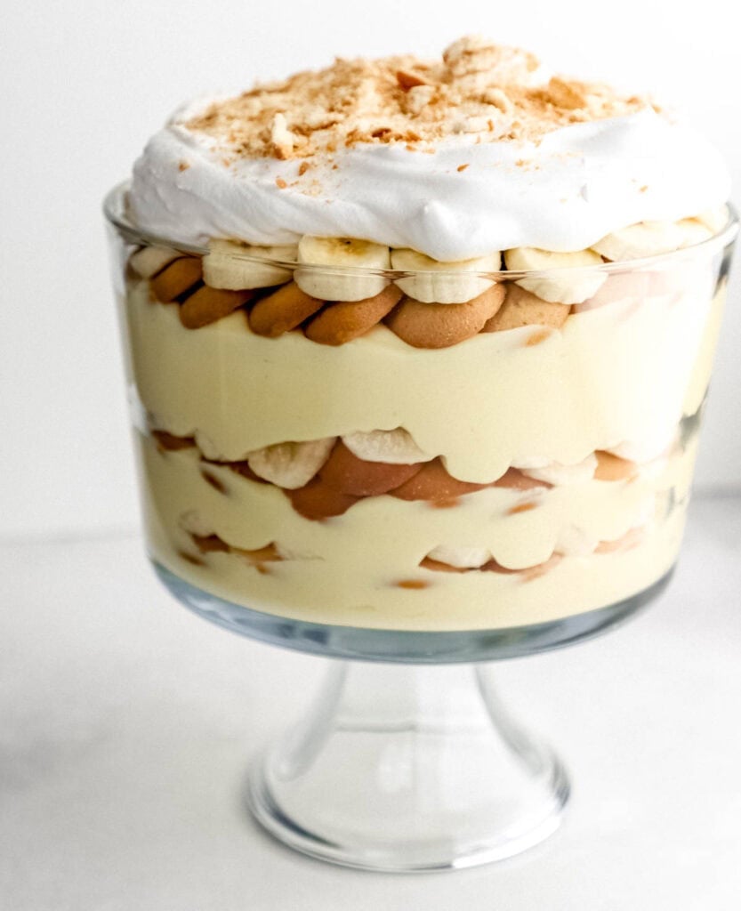 Close up front view of finished banana pudding in glass trifle dish on white surface.