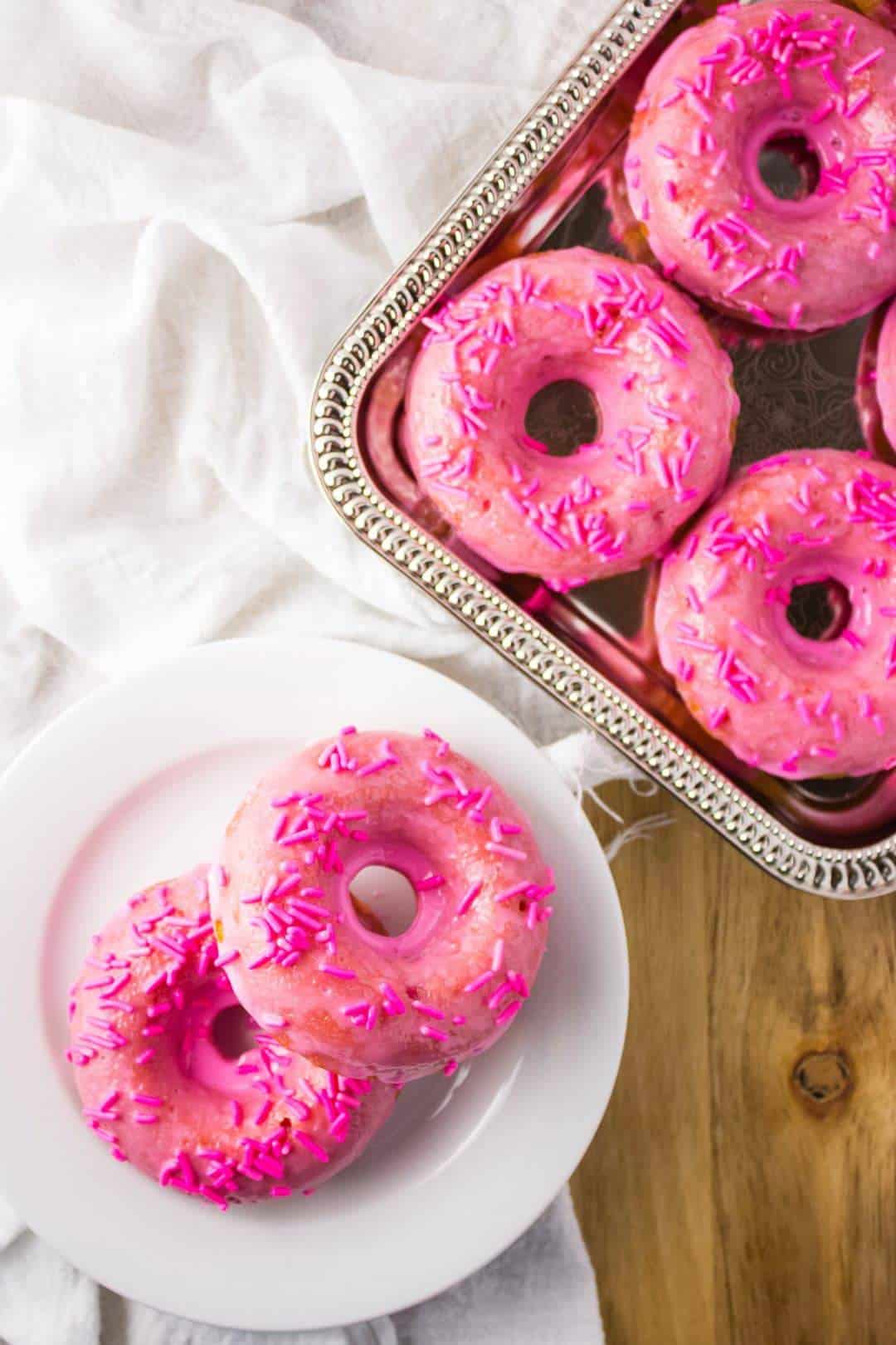 Overhead view of finished donuts on white plate and silver tray. 