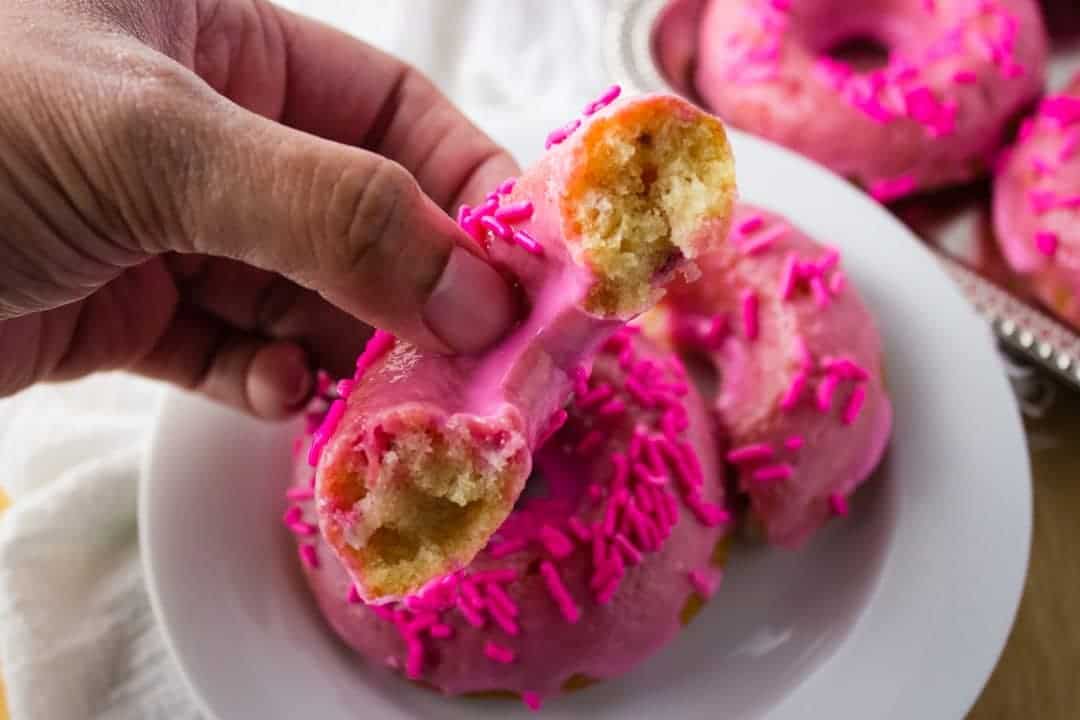 Close up of hand holding piece of donut over plate. 