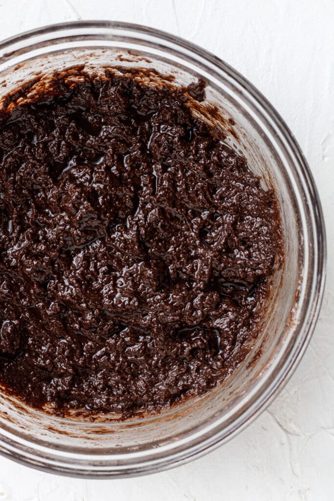glass mixing bowl with dry and wet ingredients combined together to make brownie recipe.