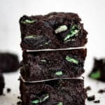 close up side view three square cut fudgy mint brownies stacked on top of each other.