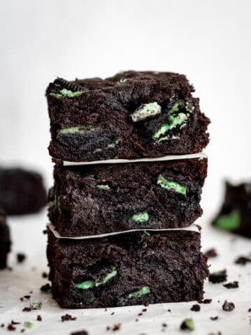 close up side view three square cut fudgy mint brownies stacked on top of each other.