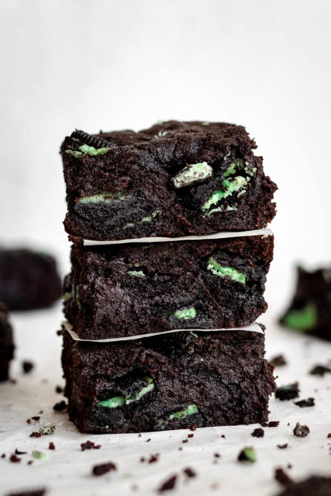 close up side view three square cut fudgy mint brownies stacked on top of each other.