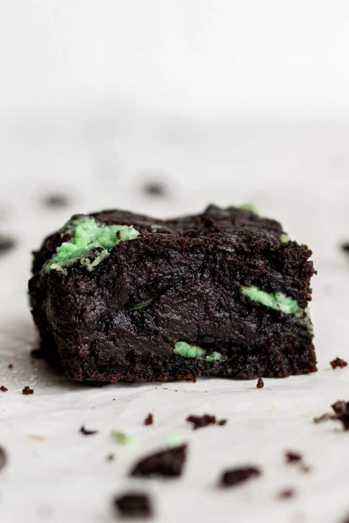 close up side view single brownie cut into a square on white surface.