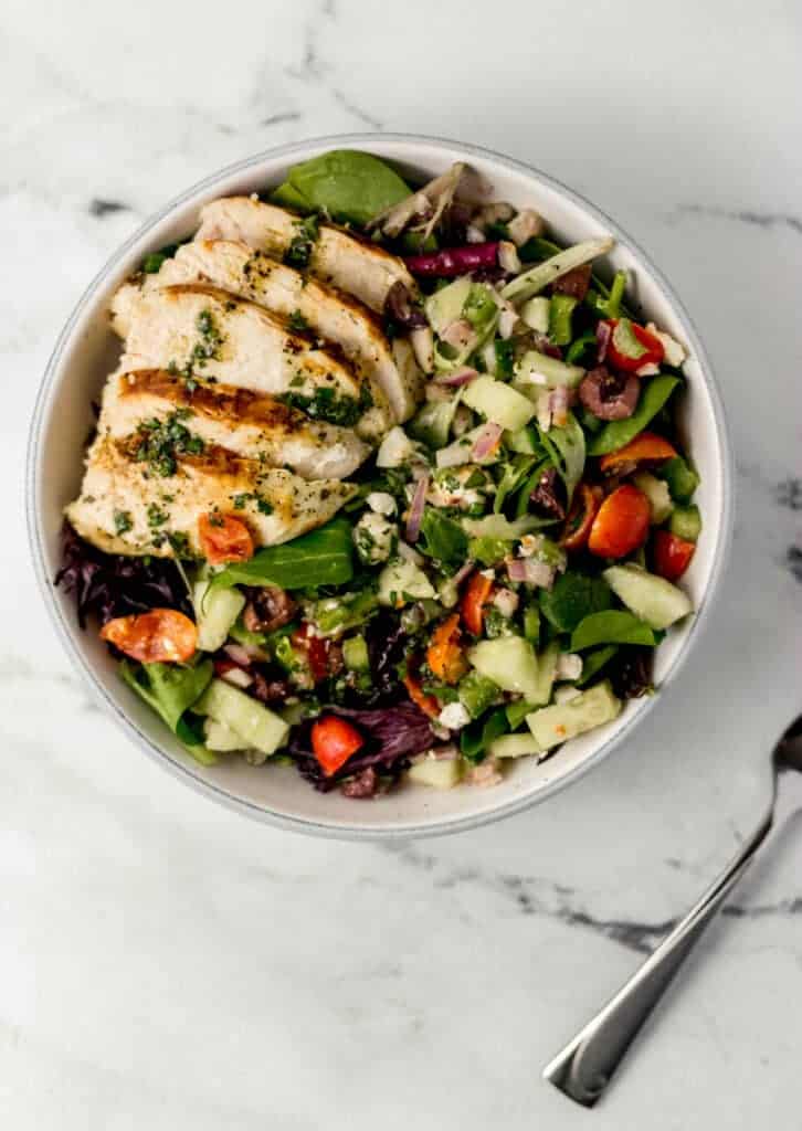 overhead view of finished salad beside a fork on marble surface 