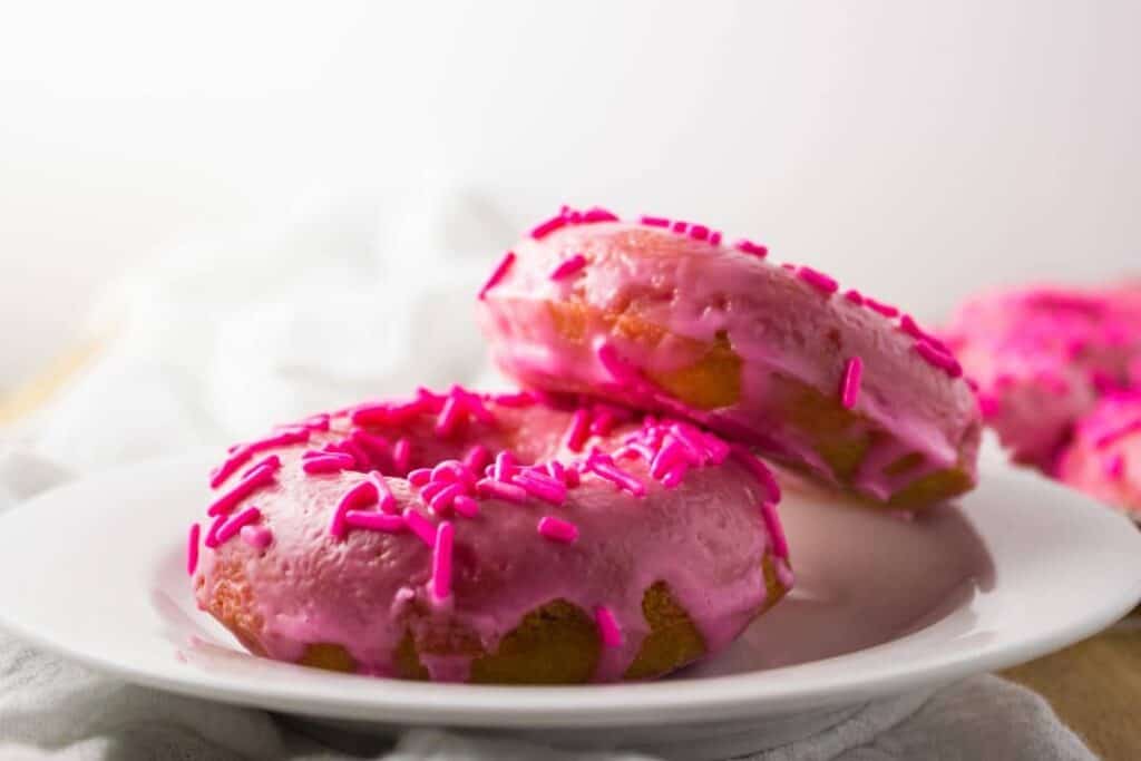 close up side view of two doughnuts on white plate 