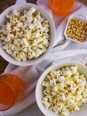 popcorn in two white bowls beside cup of orange soda