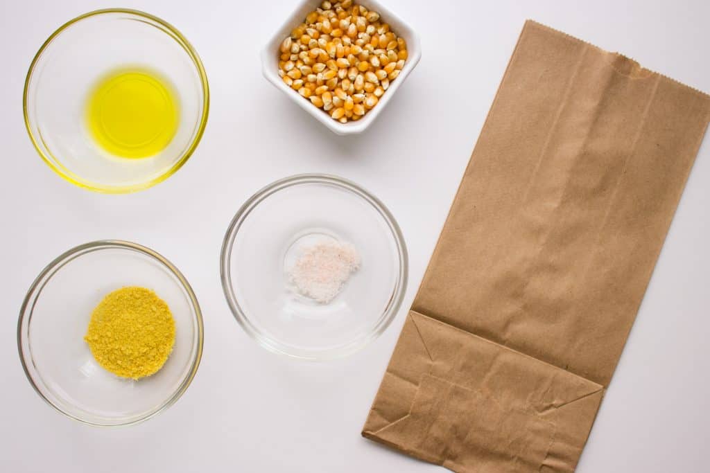 overhead view of ingredients needed to make popcorn in separate bowls on white surface