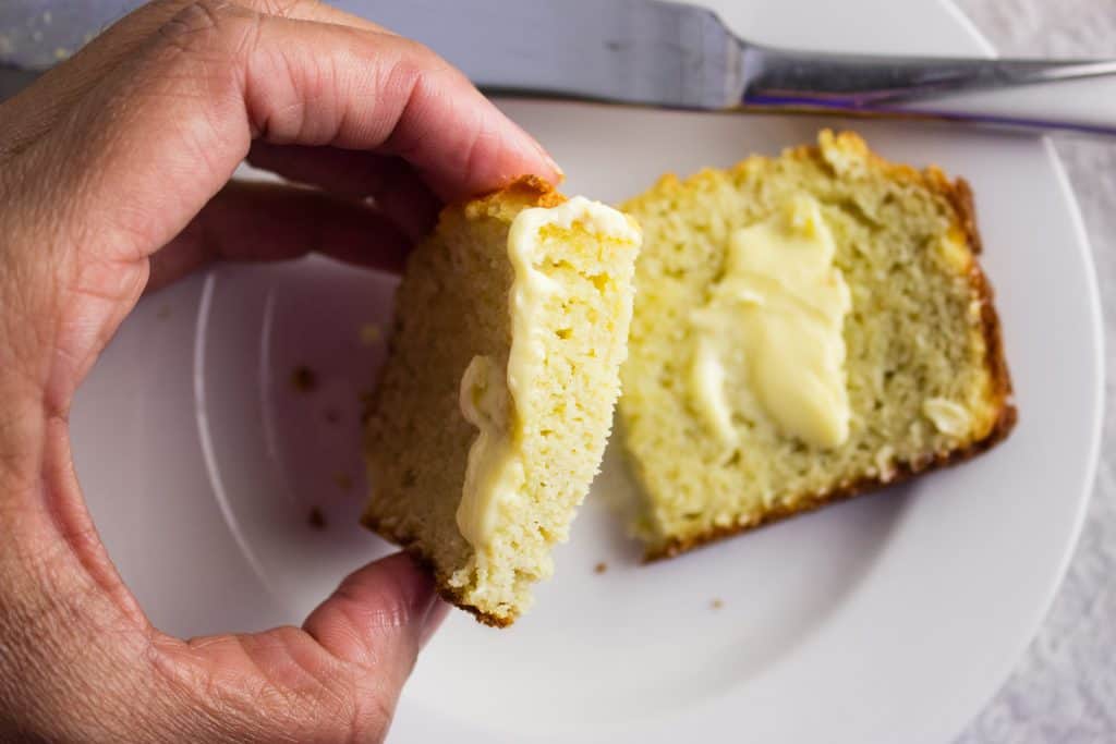 Hand holding one slice of almond coconut flour bread topped with butter and cut in half